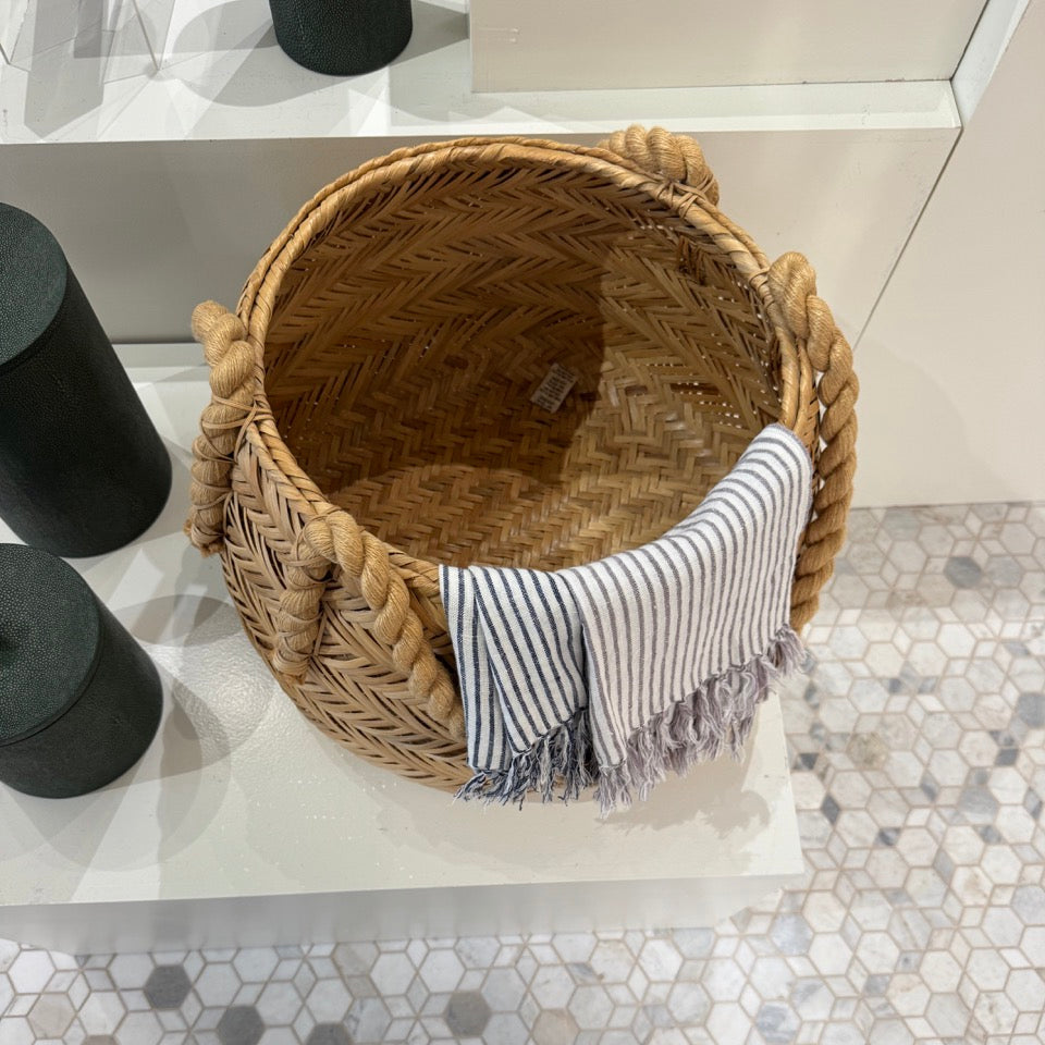 Woven basket with a striped towel on a white surface, with a person's feet visible at the bottom.