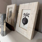 Two framed artworks on a shelf with a neutral background