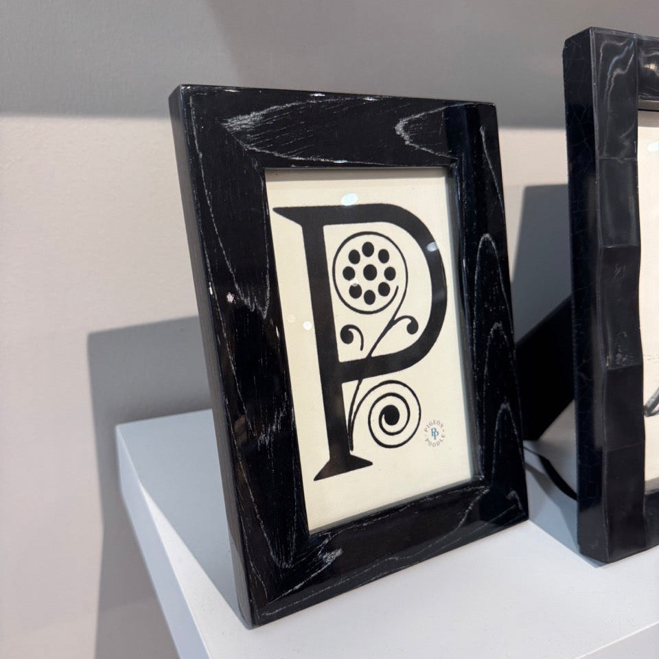 Black-framed decorative item with a letter 'P' design on a white surface.
