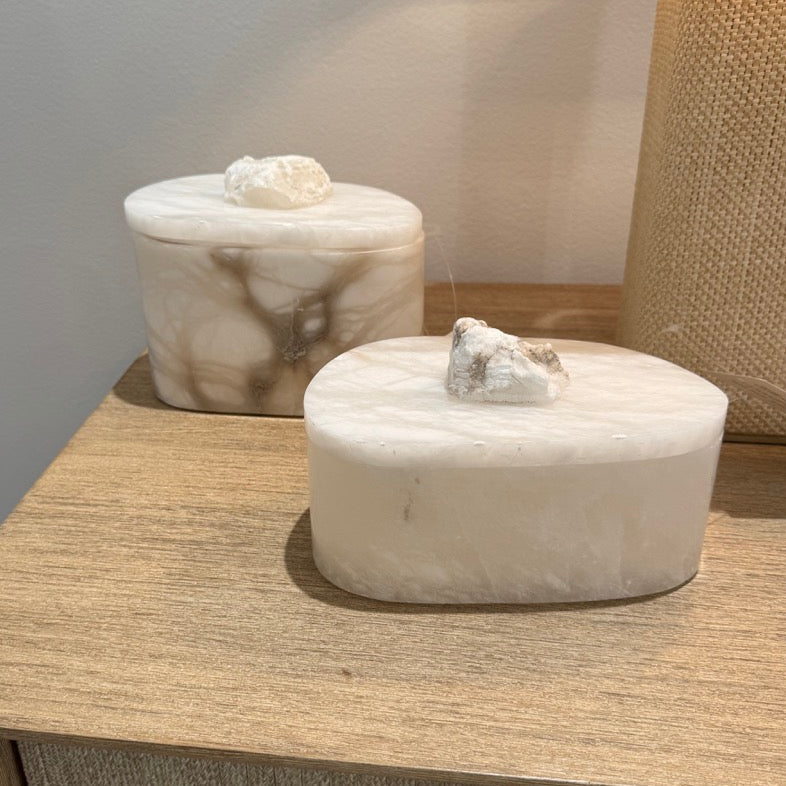 Two marble containers on a wooden nightstand with a lamp in the background.