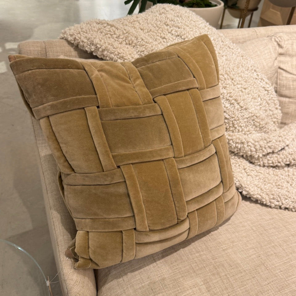 Beige woven pillow on a sofa with a blurred indoor setting