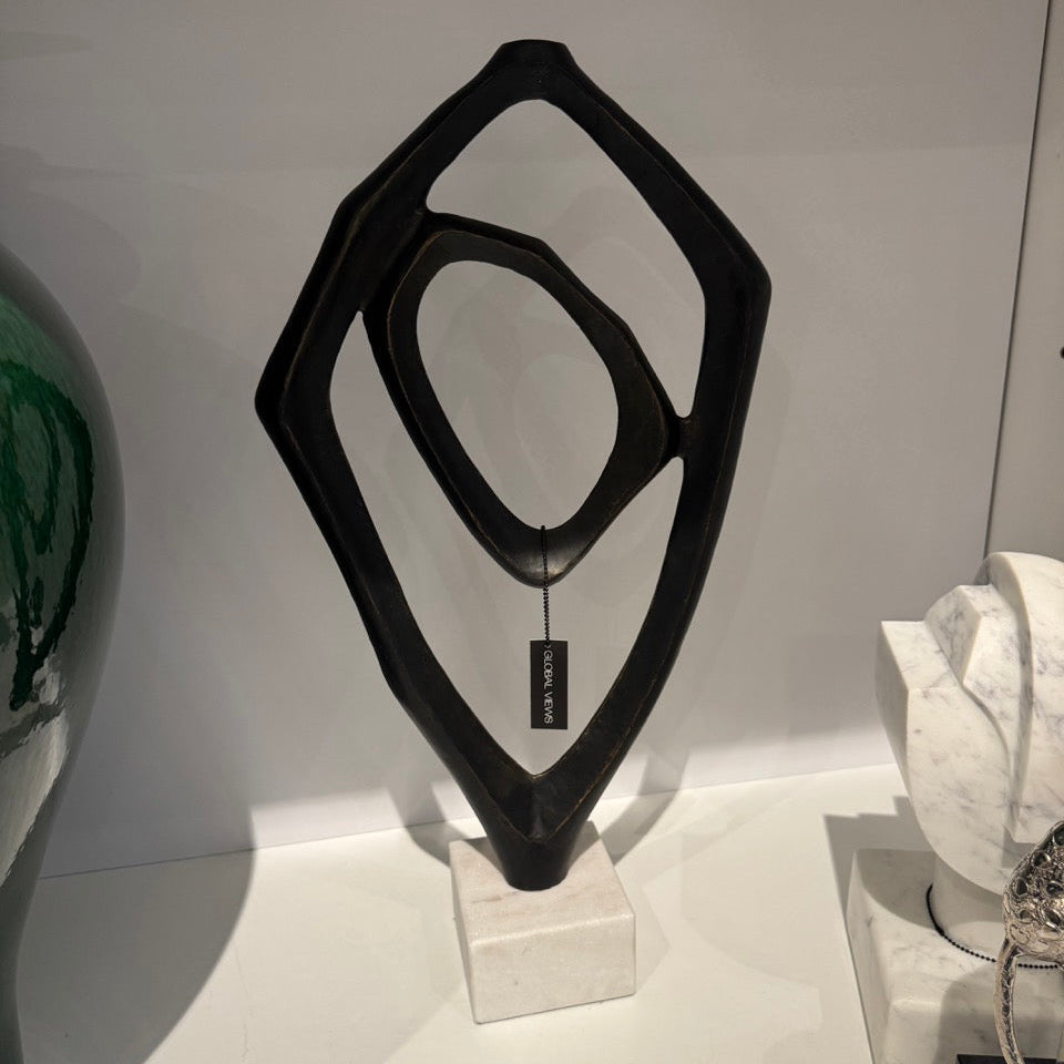 Black abstract sculpture on a white surface with a white wall background
