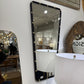 Decorative mirror with black frame and decorative studs on a white wall.