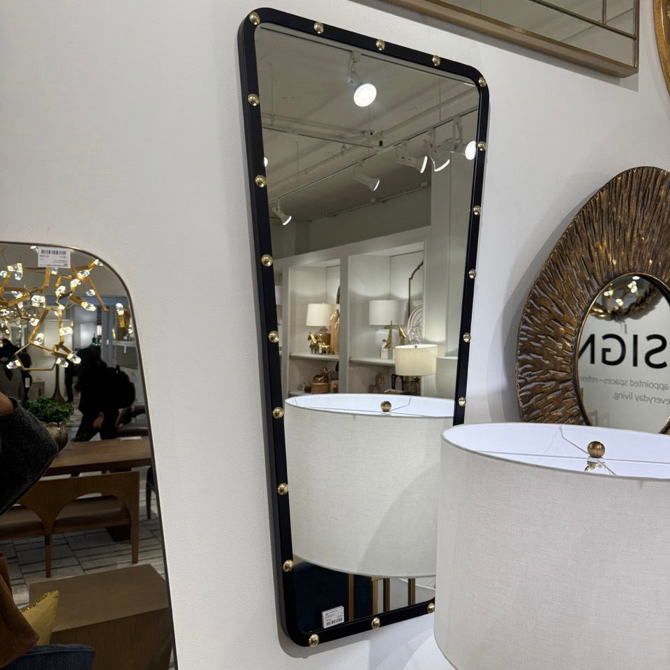 Decorative mirror with black frame and decorative studs on a white wall.