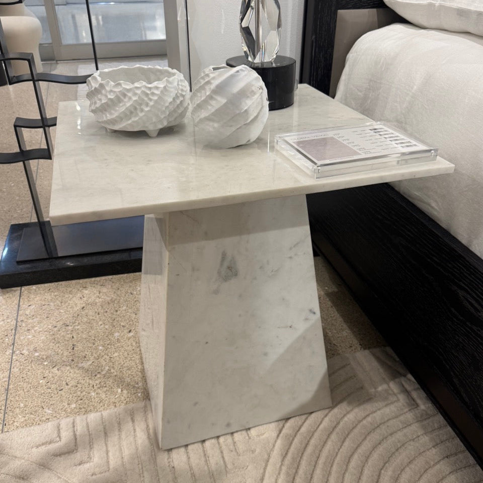 White marble side table in a room setting with a bed and decor items.