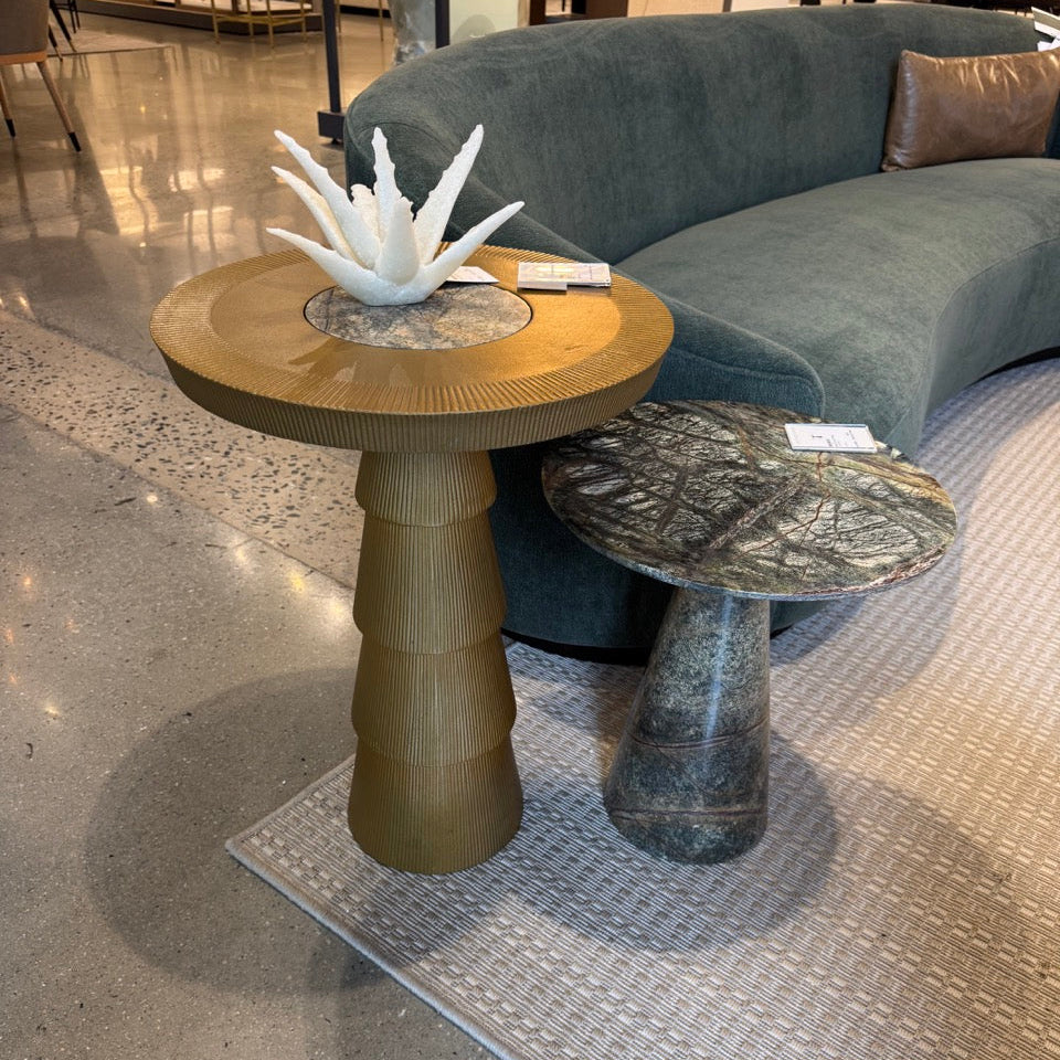 Two unique side tables in a showroom setting with a gray sofa.