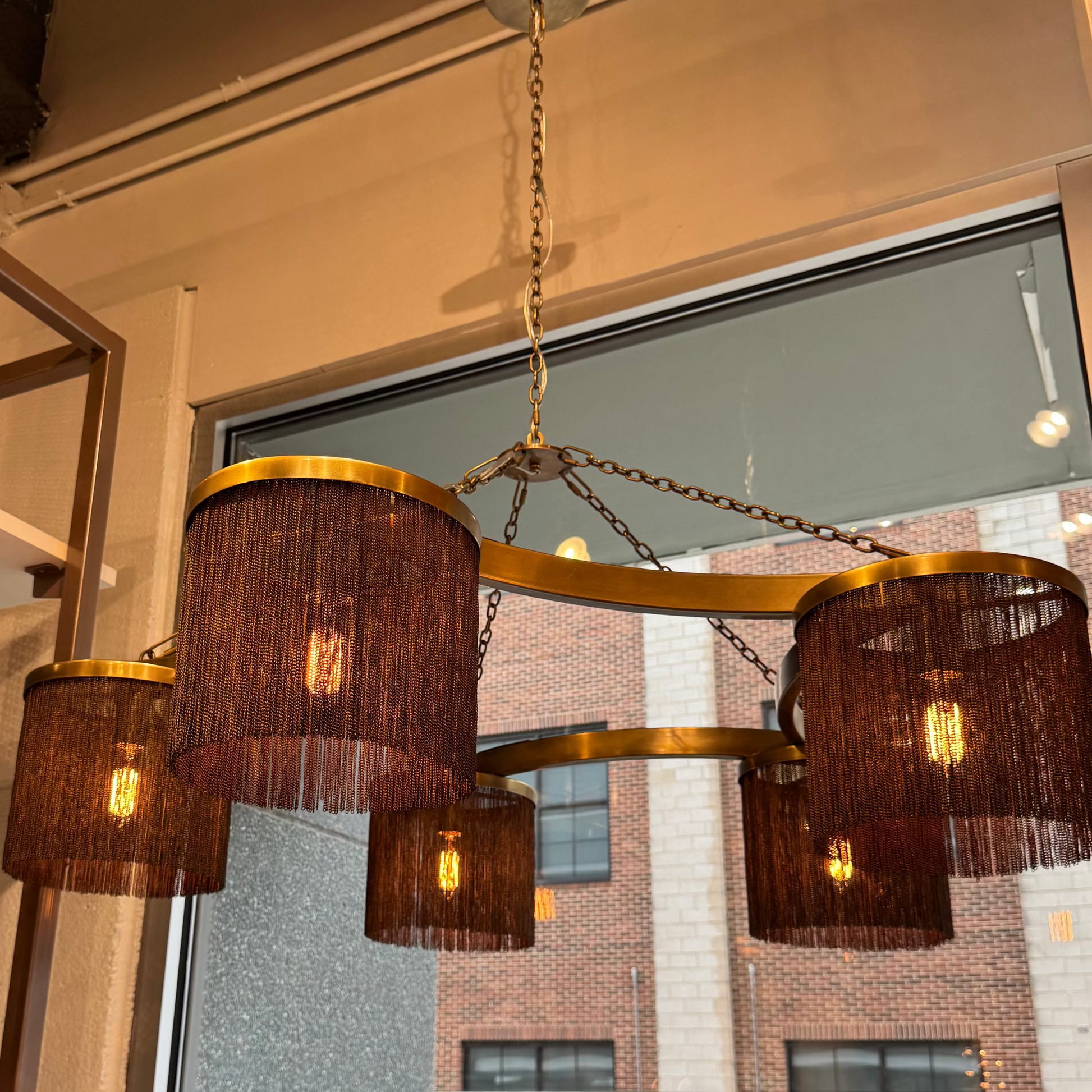 Chandelier with woven design hanging in front of a window with a view of a building.