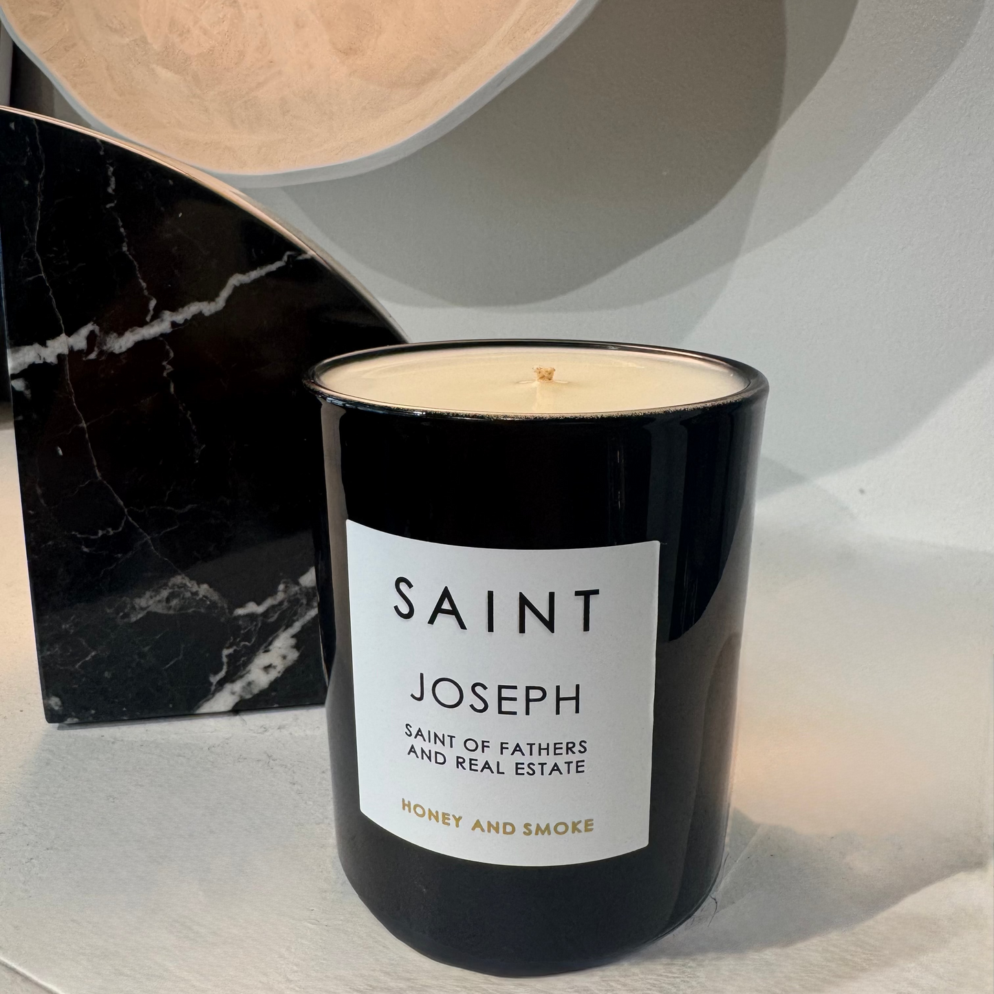 Black candle with a white label on a light surface, with a marble object in the background.