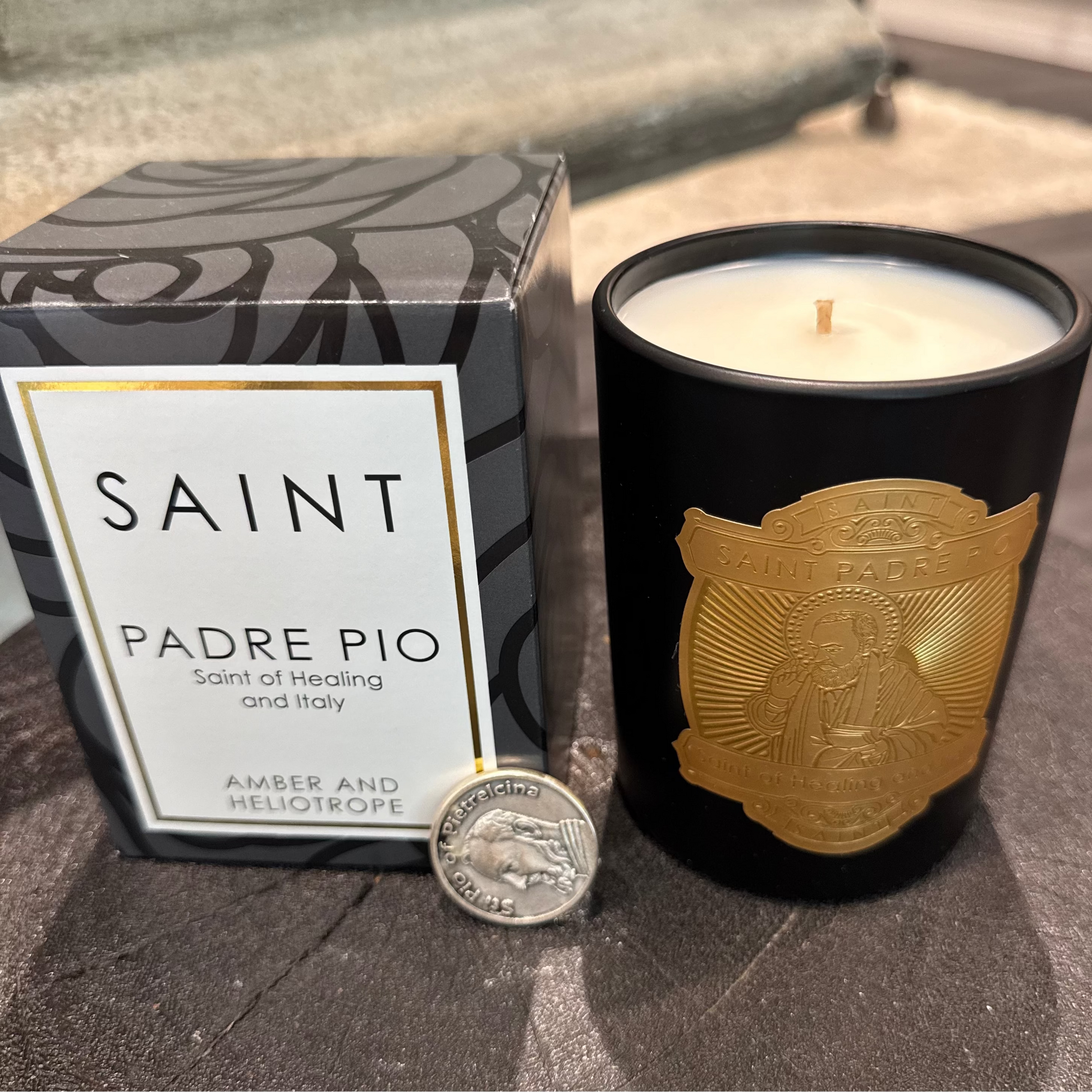 Candle with gold emblem and packaging labeled 'Saint Padre Pio' on a stone surface.