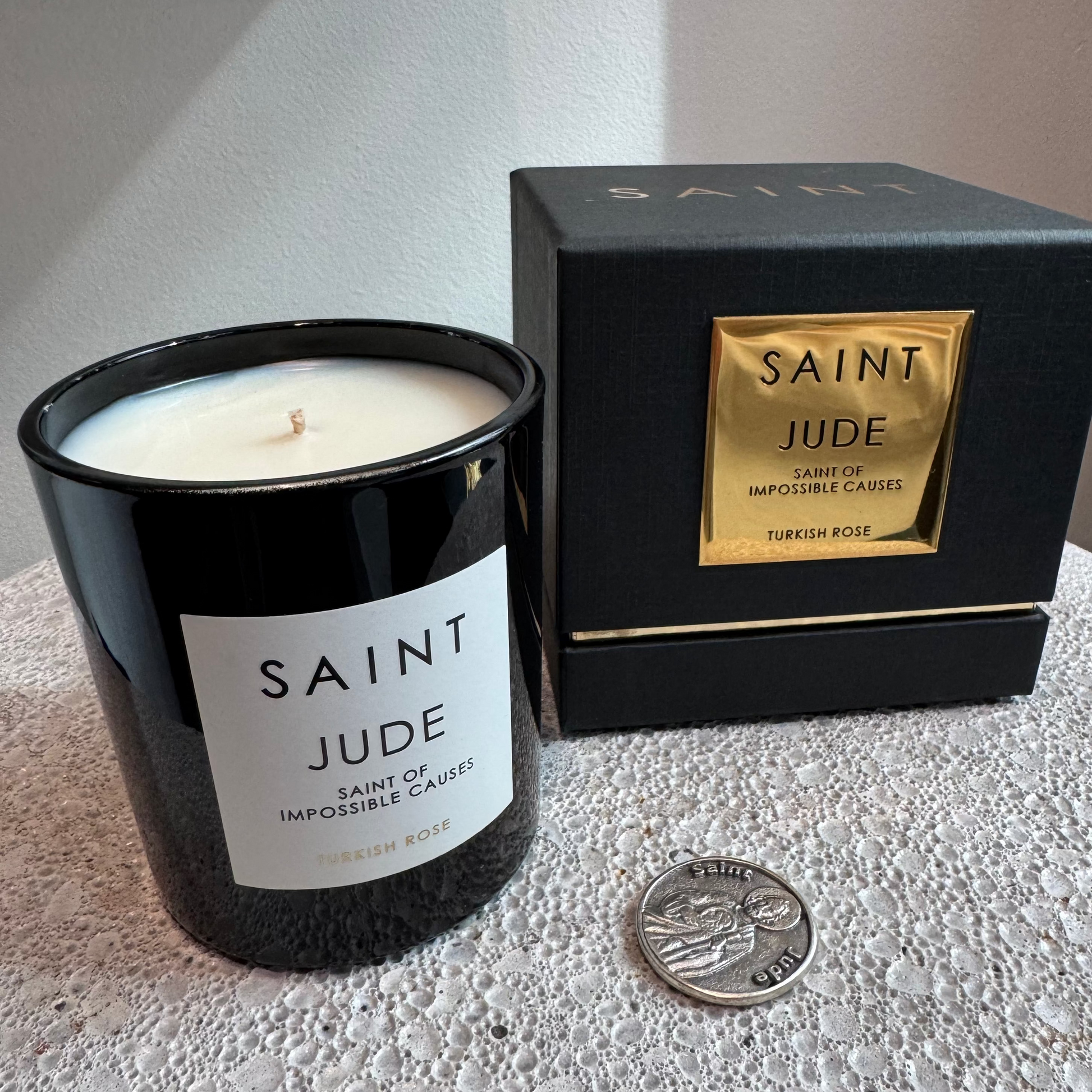 Black candle labeled 'Saint Jude' next to its packaging on a textured surface.
