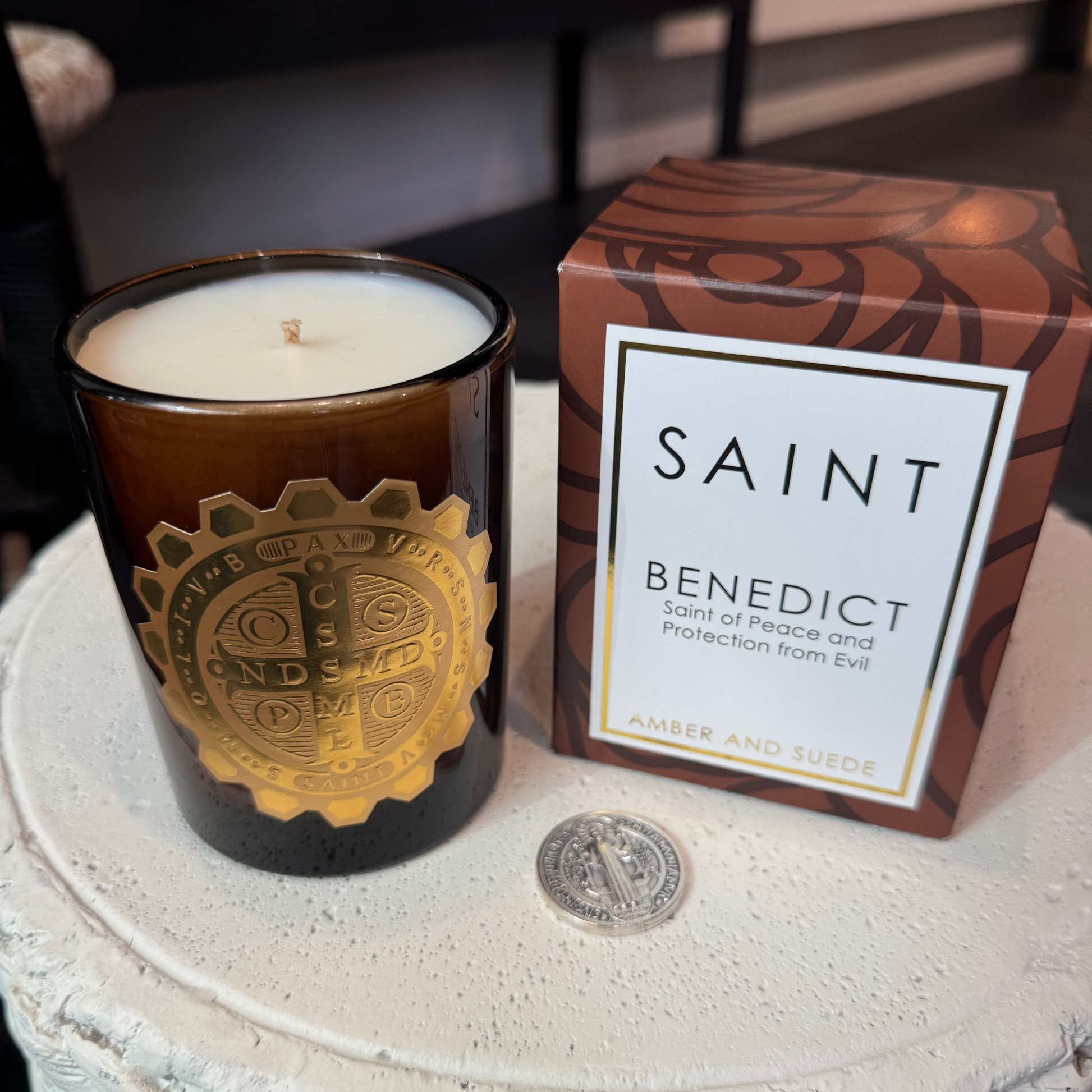 Candle with decorative label and 'Saint Benedict' packaging on a textured surface.