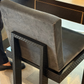 Gray cushioned stool with black woven base in a room setting