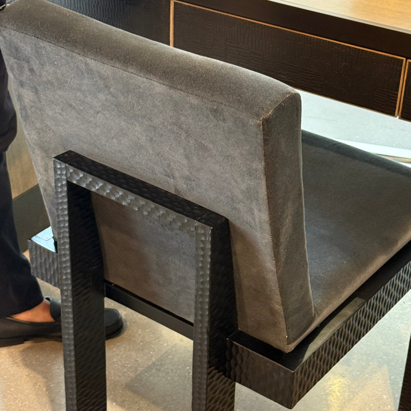 Gray cushioned stool with black woven base in a room setting