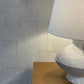 Gray textured lamp on a wooden surface with a stone wall background