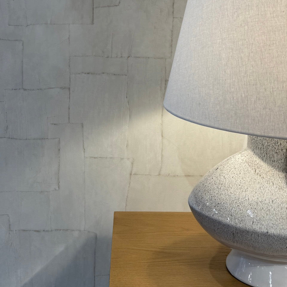 Gray textured lamp on a wooden surface with a stone wall background