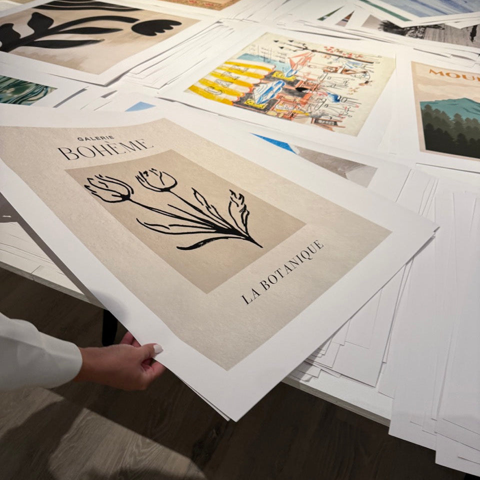 Collection of art prints on a table with a hand holding one print.
