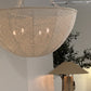 Woven pendant light fixture hanging in a room with a plant and other lamps.