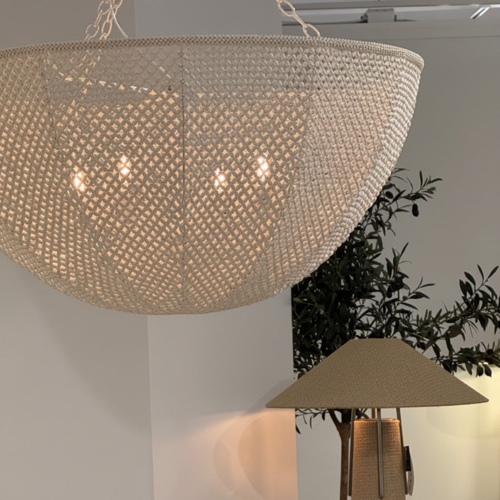 Woven pendant light fixture hanging in a room with a plant and other lamps.