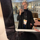 Person taking a mirror selfie in a store with a visible name tag.