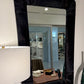 Black-framed mirror on a white wall with a lamp and chair reflection