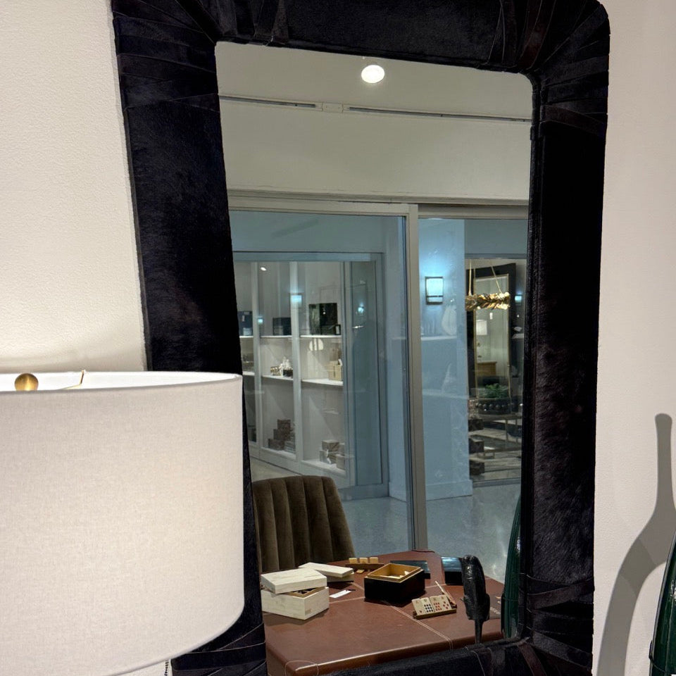Black-framed mirror on a white wall with a lamp and chair reflection