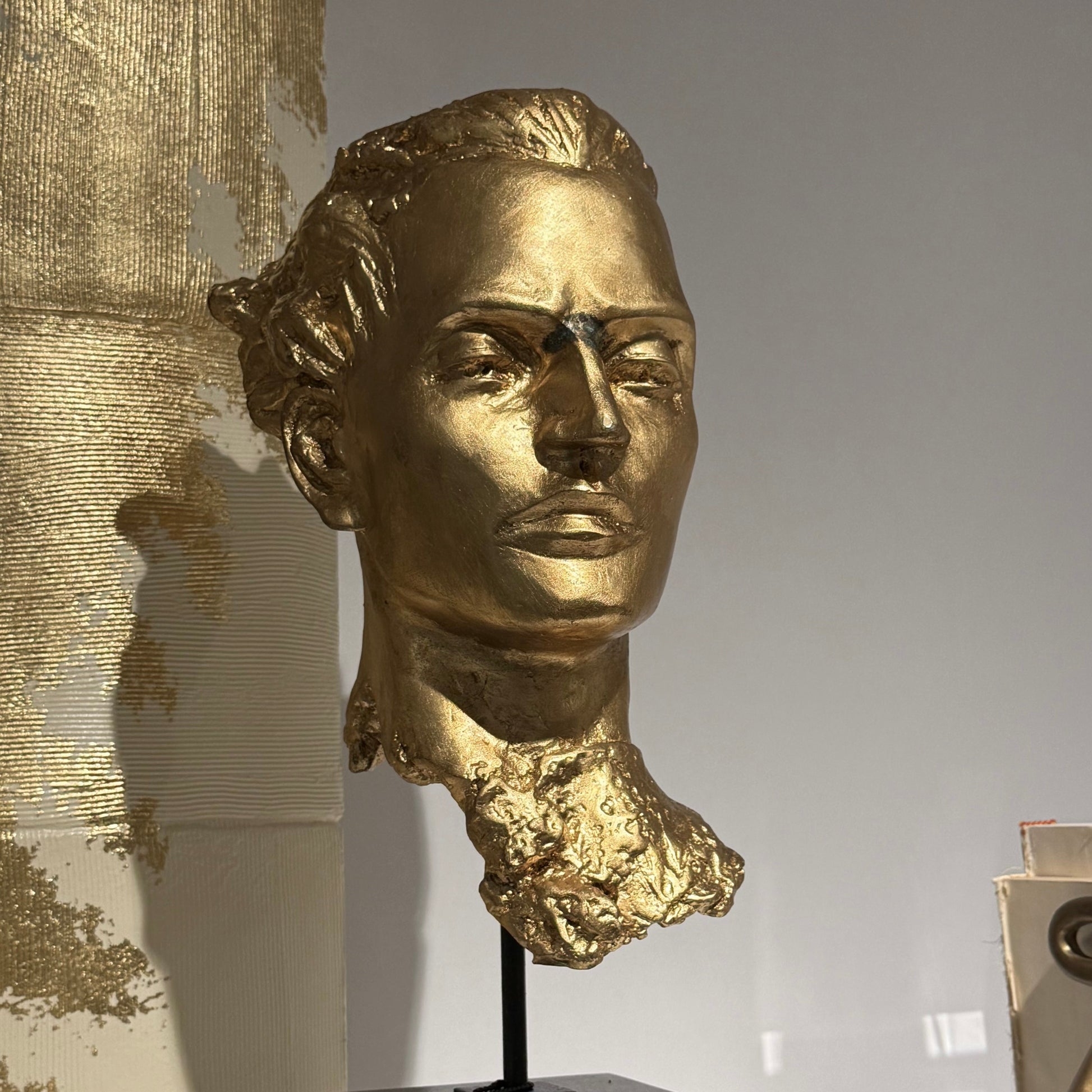 Gold bust of a man on a black pedestal against a neutral background