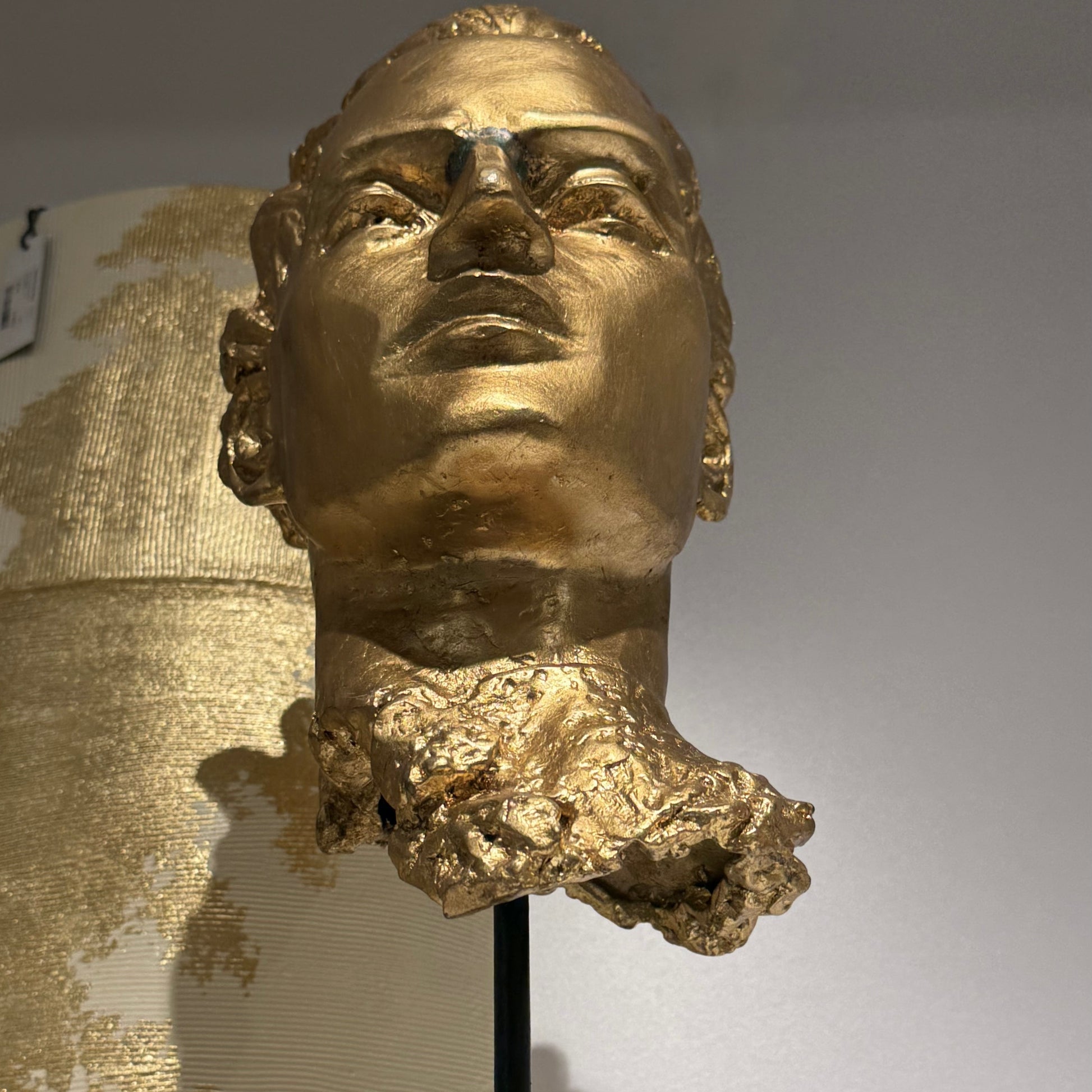 Gold bust on a stand against a neutral background