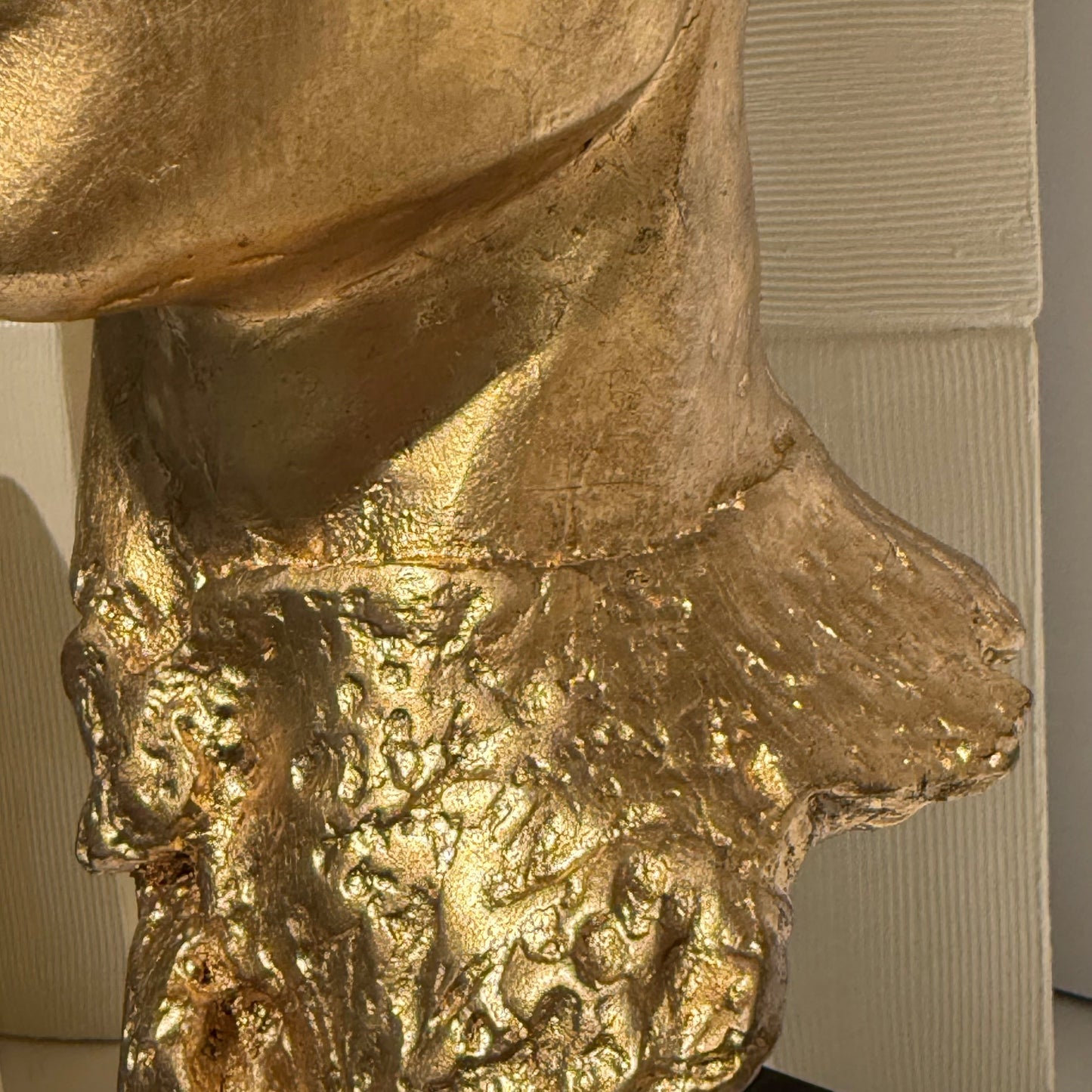 Gold-colored bust of a person with a neutral expression on a plain background