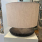Table lamp with a beige shade and ribbed black base on a white pedestal