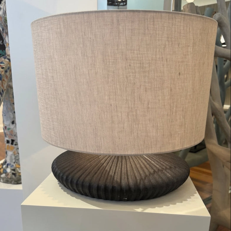 Table lamp with a beige shade and ribbed black base on a white pedestal