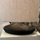 Table lamp with a textured beige shade and ribbed black base on a white surface.