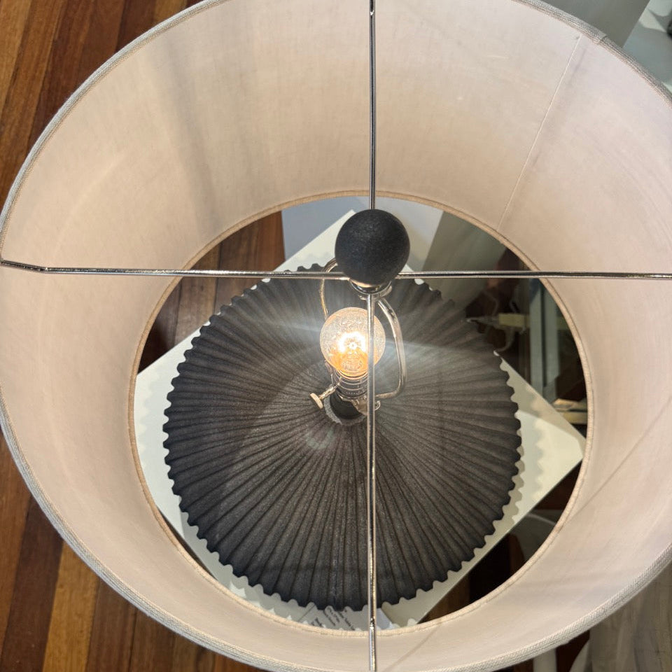 Ceiling light fixture with a white lampshade and dark ribbed design on a wooden floor.