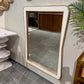 Rectangular mirror with a wooden frame on a wall in a room with a plant and other decor items.