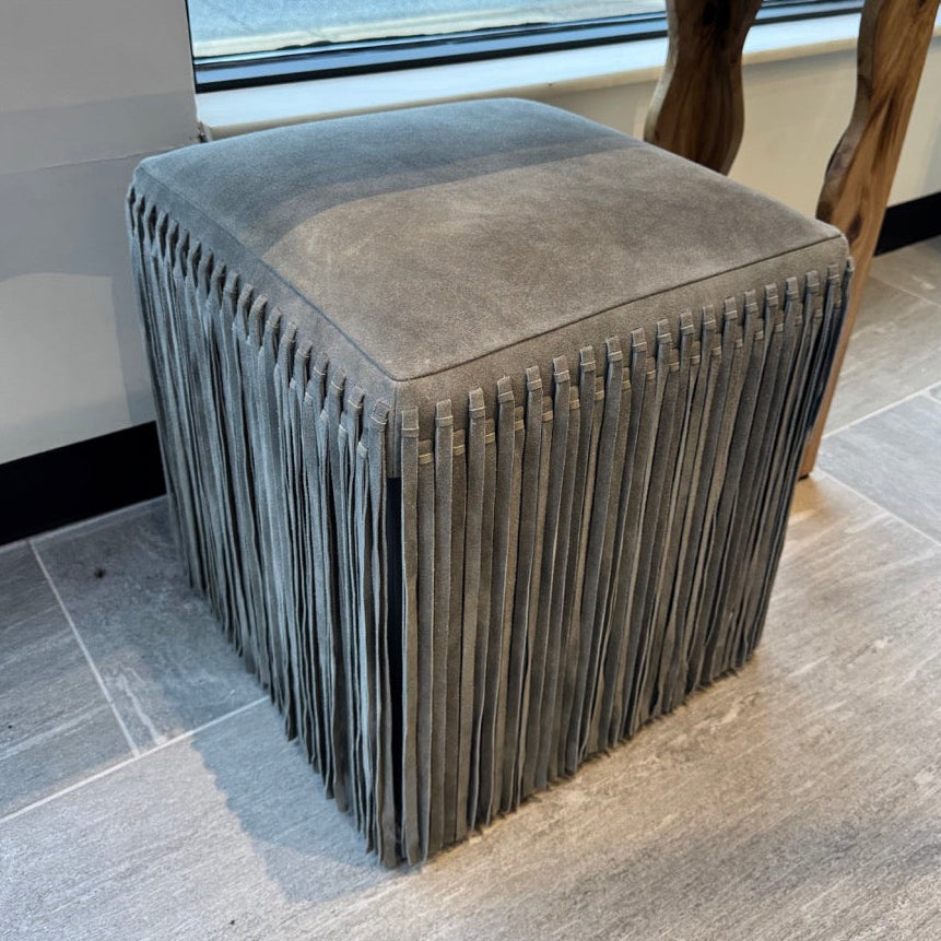 Gray textured stool in front of a wooden table with a window in the background