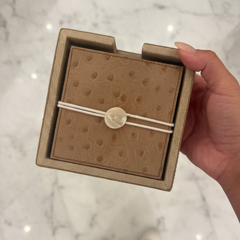 Brown textured jewelry box with a white tag held by a hand on a reflective surface.