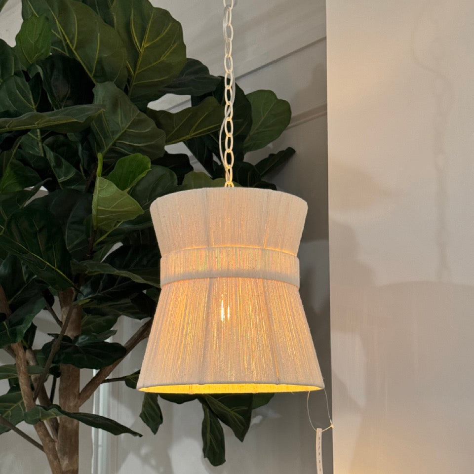 Pendant light with pleated shade hanging in a room with a plant.