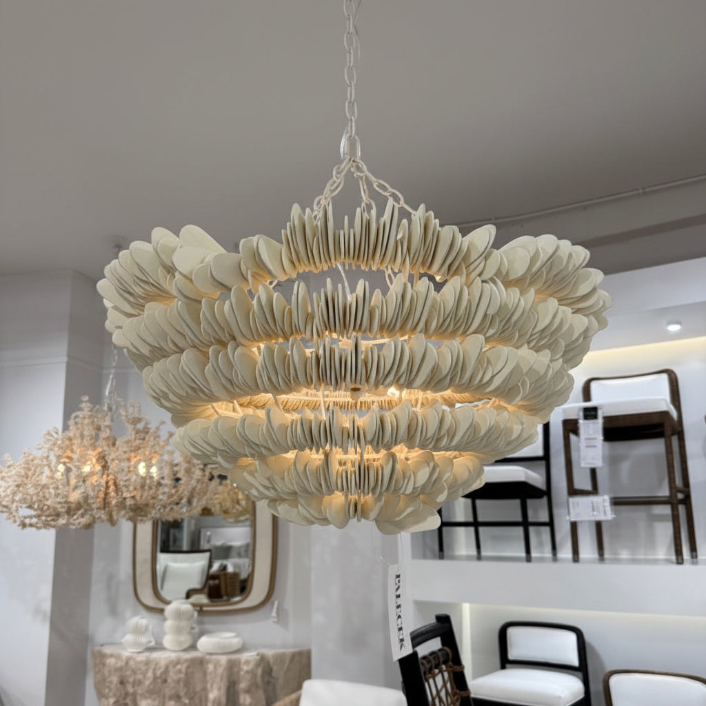 Large decorative chandelier hanging in a showroom with furniture and mirrors.