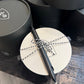 Black pen tied with string on a white circular card, surrounded by black cylindrical containers.