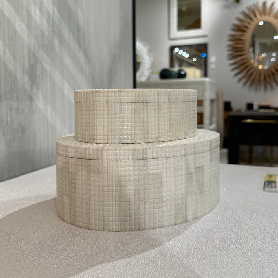 Two round, textured boxes on a surface with a blurred interior background