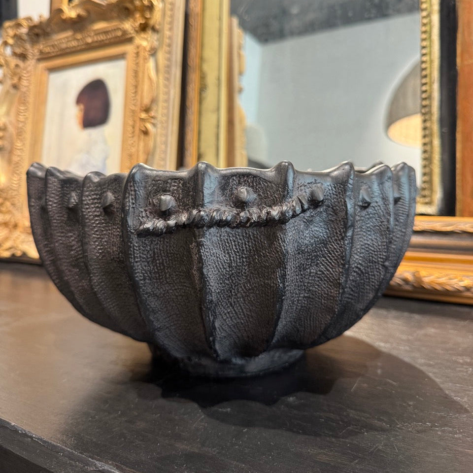 Decorative black shell-shaped bowl on a dark surface with gold-framed mirrors in the background.
