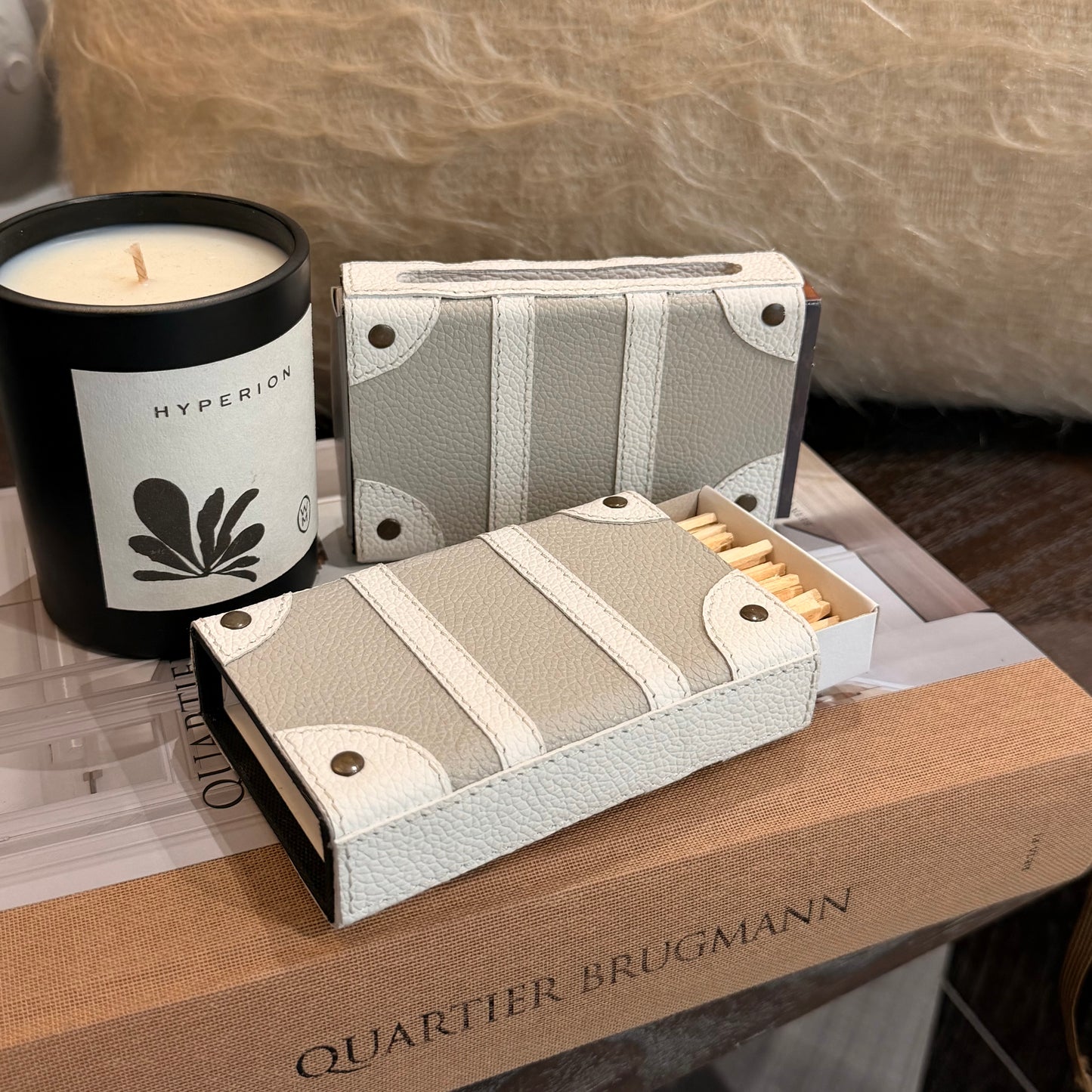 A set of two decorative matches styled like a book, featuring a textured light gray and white cover with faux leather-like panels and brass rivets. One matchbox is closed, and the other is open, showing yellow matches inside.