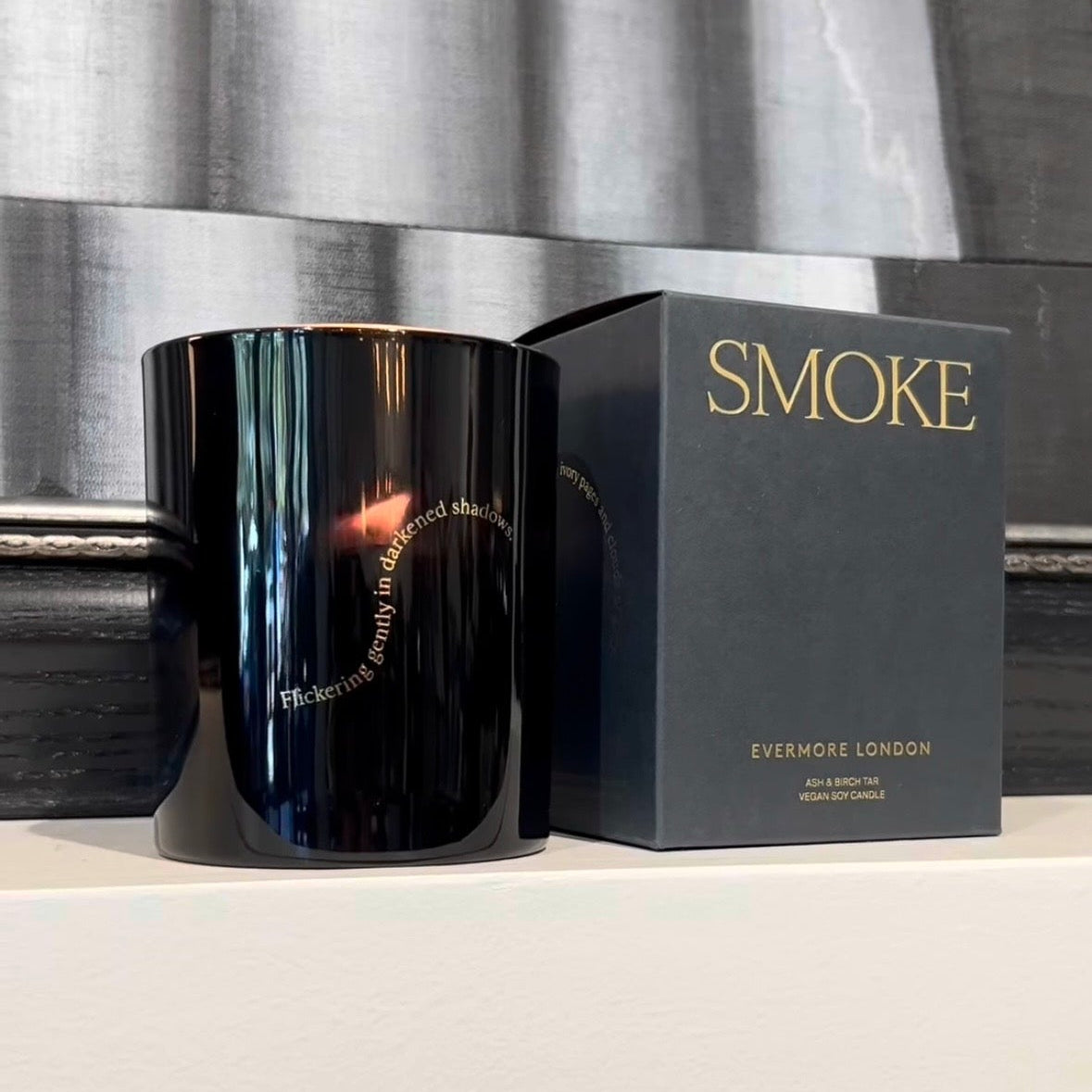 Black candle with 'Smoke' packaging in front of a curtain