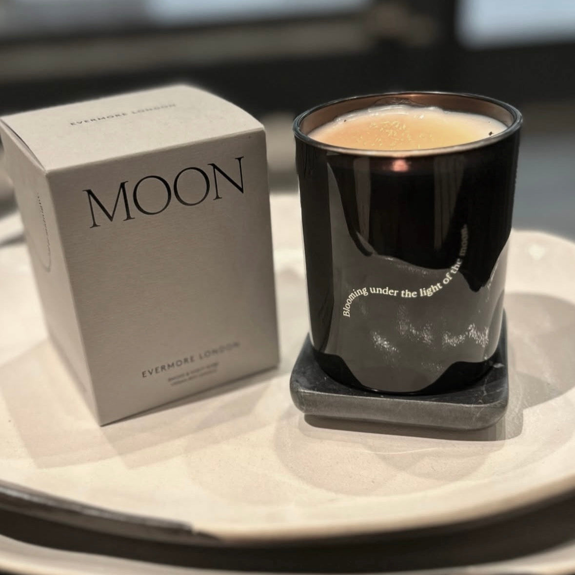 Black candle in a glass container with 'MOON' branding next to a box on a table.