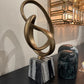 Decorative sculpture with interlocking rings on a marble base in an elegant interior setting.