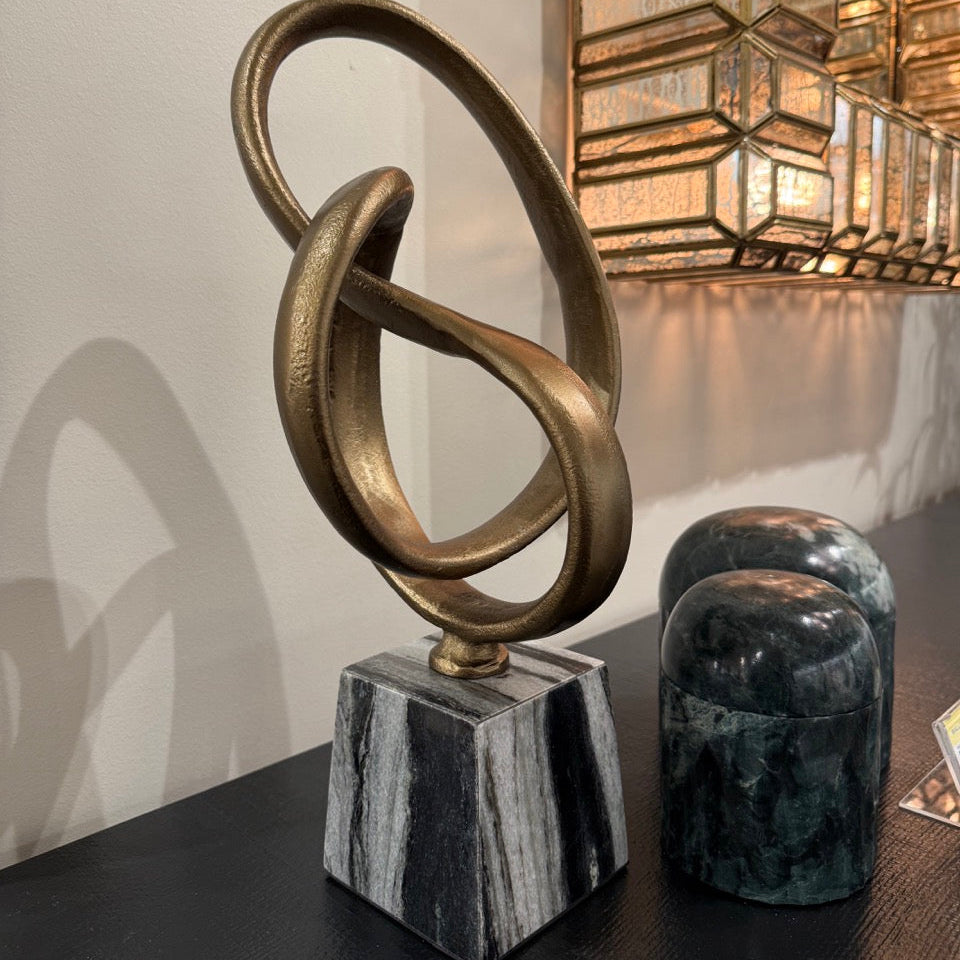 Decorative sculpture with interlocking rings on a marble base in an elegant interior setting.