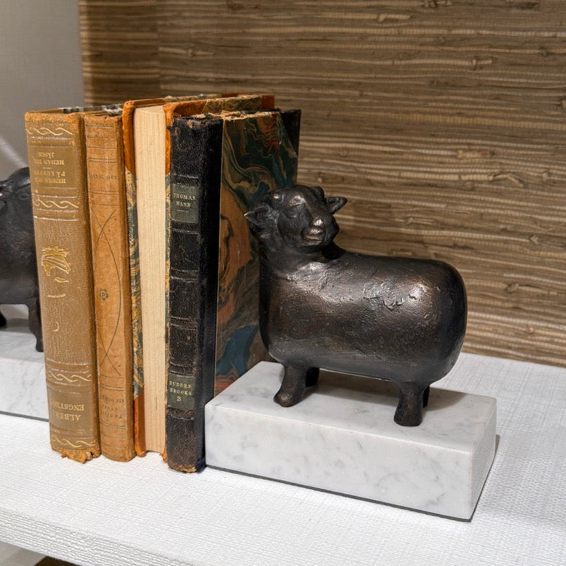 Decorative bull bookend on a shelf with books against a wooden wall.