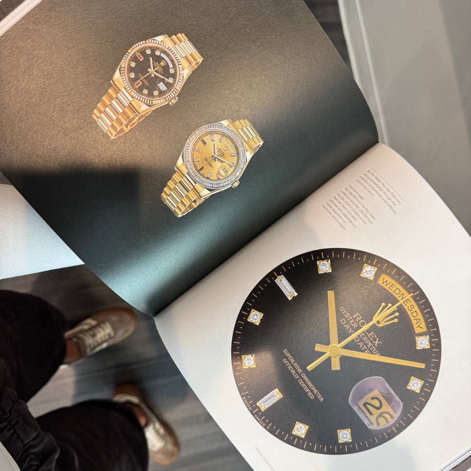 Two gold watches on an open book with a close-up of a watch face.