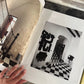 Person holding a framed black and white print of a room with a checkered floor.