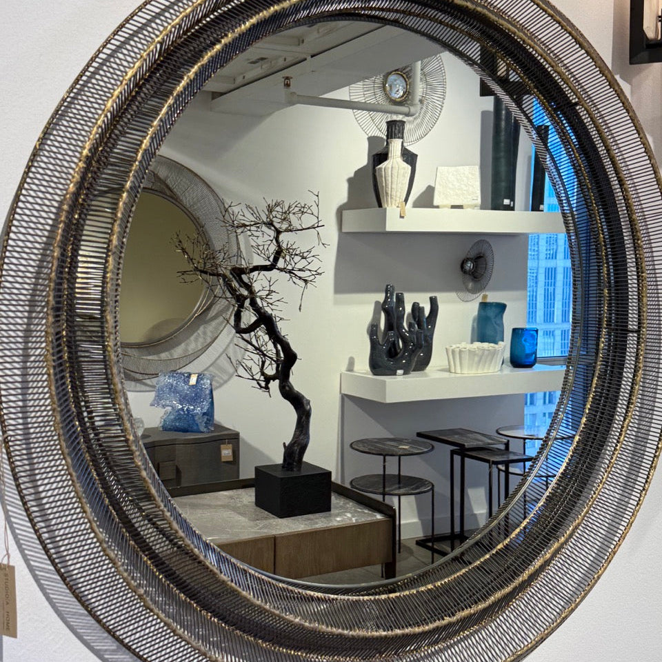 Round decorative mirror with a black wireframe design on a white wall.