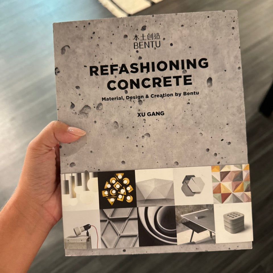 Book titled 'Refashioning Concrete' held by a hand on a reflective surface.